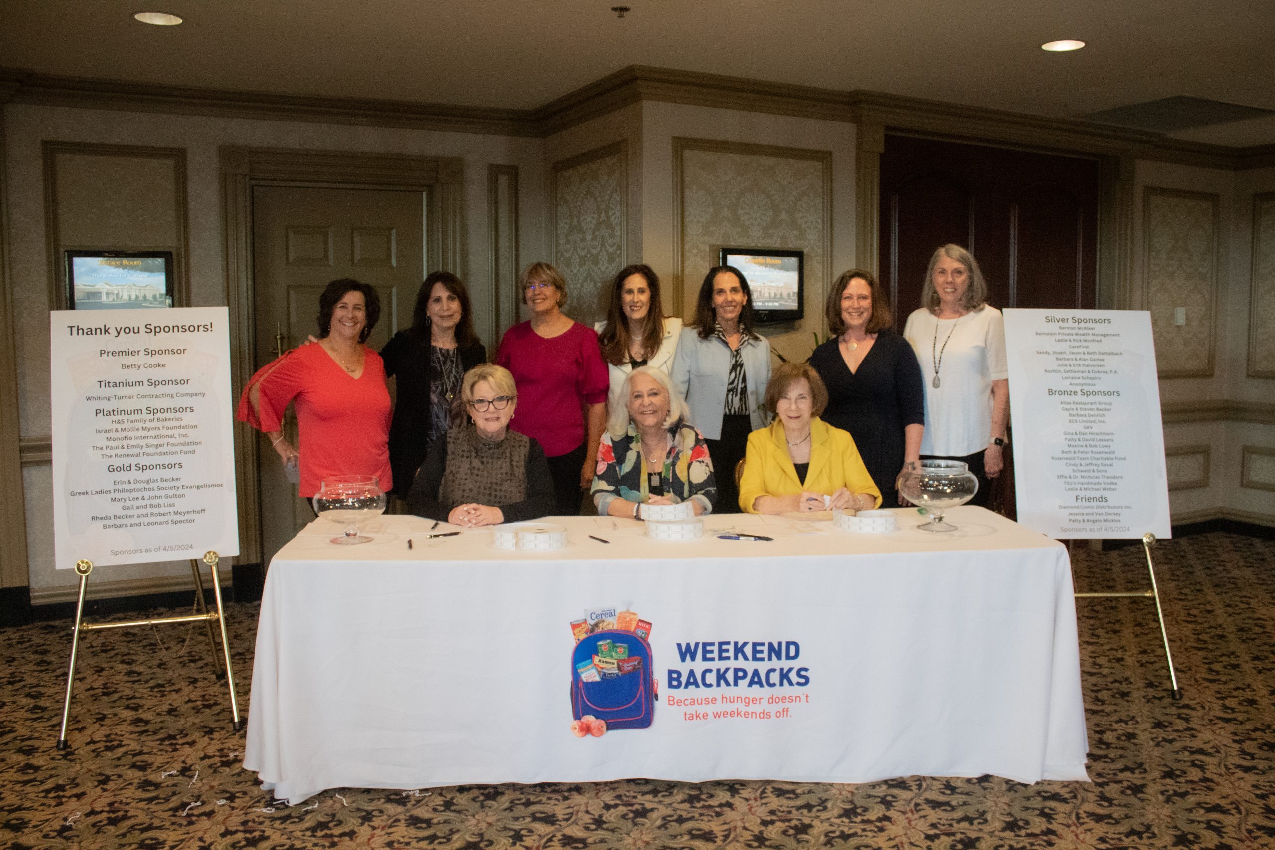 IMG_8750 - Weekend Backpacks Baltimore A group of women posed smiling behind a welcome table.